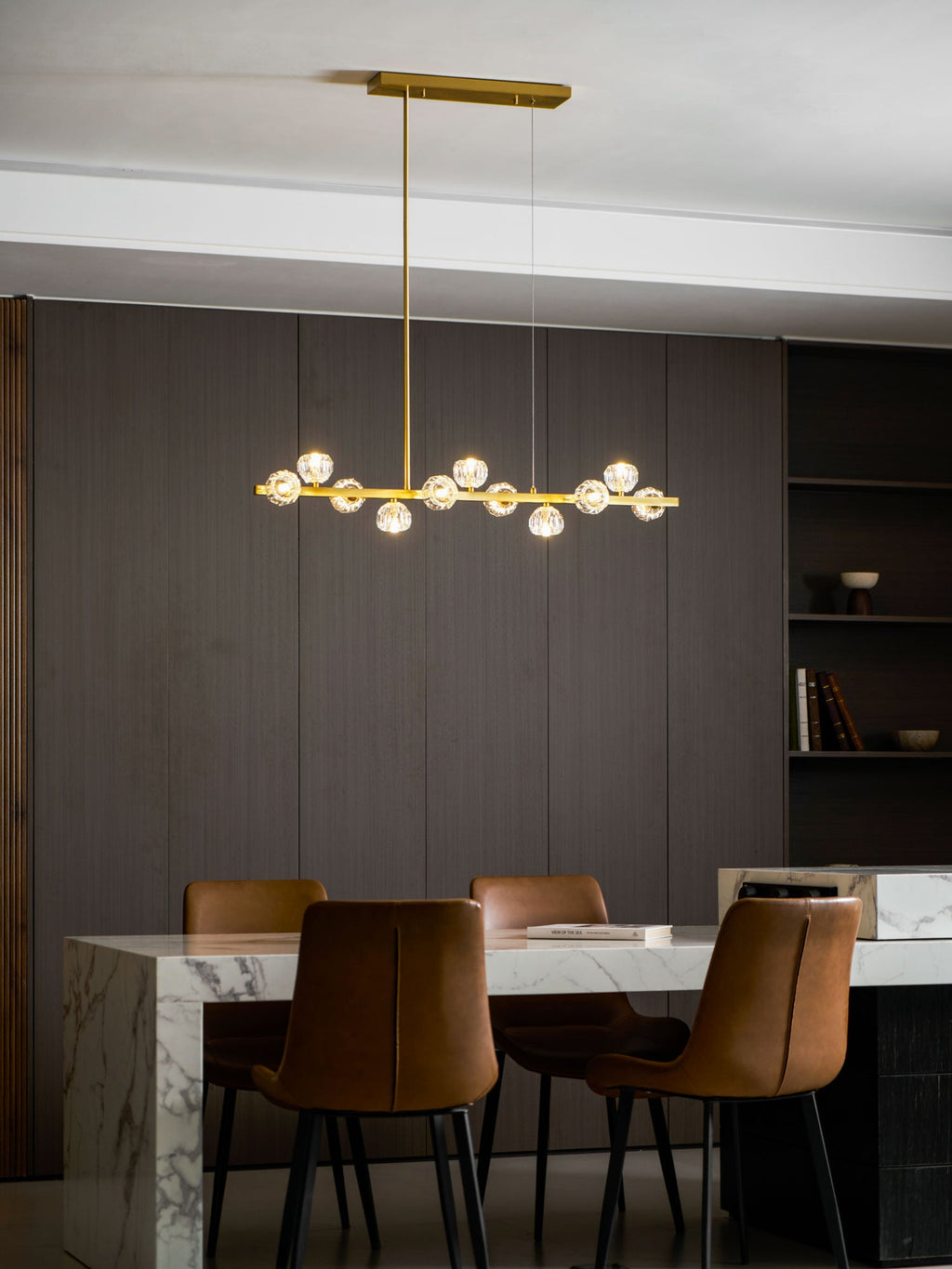 A Clérachic chandelier lit above a marble dining table with brown leather chairs and a dark panelled wall.
