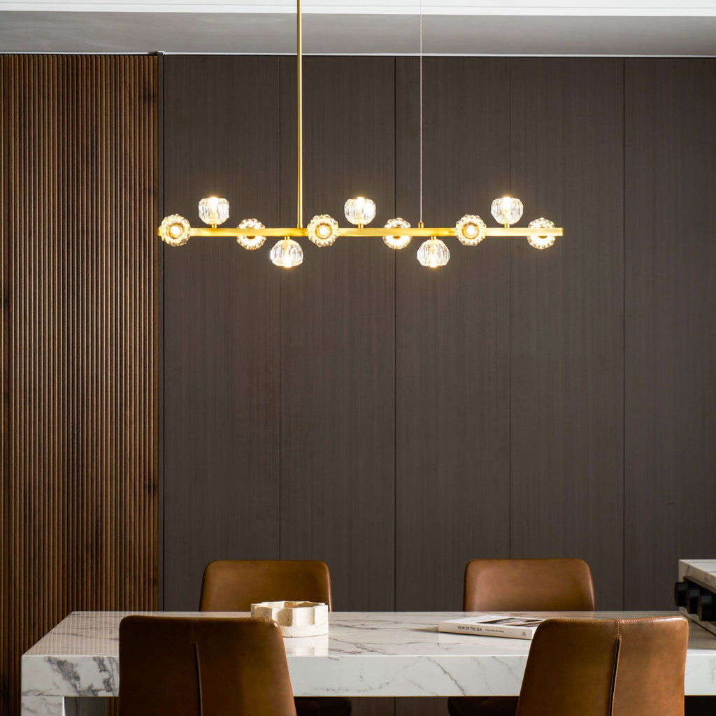 Lit crystal balls along the brass bar of a Clérachic chandelier, hung before dark wood panelling and a marble table.
