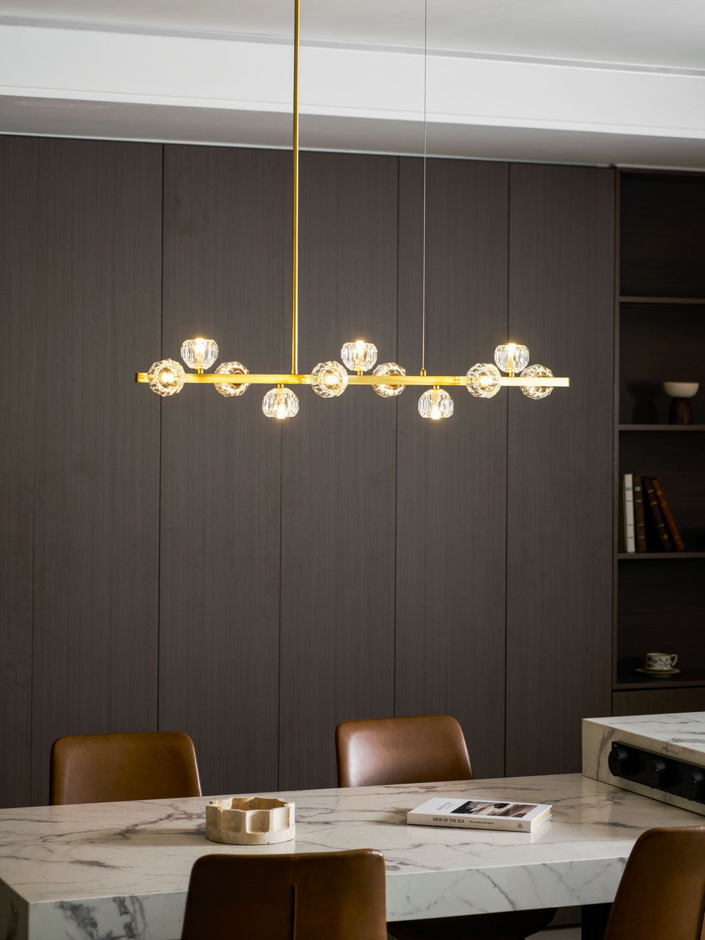 Small Clérachic chandelier lit over a marble table, with a shelf of books and a wood wall behind.