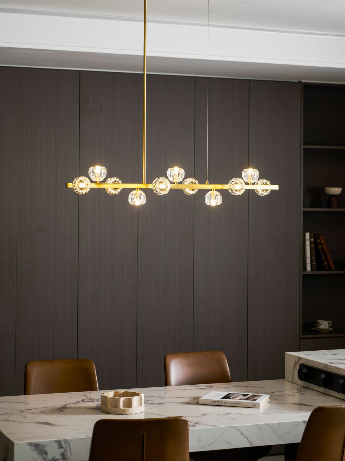 Small Clérachic chandelier lit over a marble table, with a shelf of books and a wood wall behind.