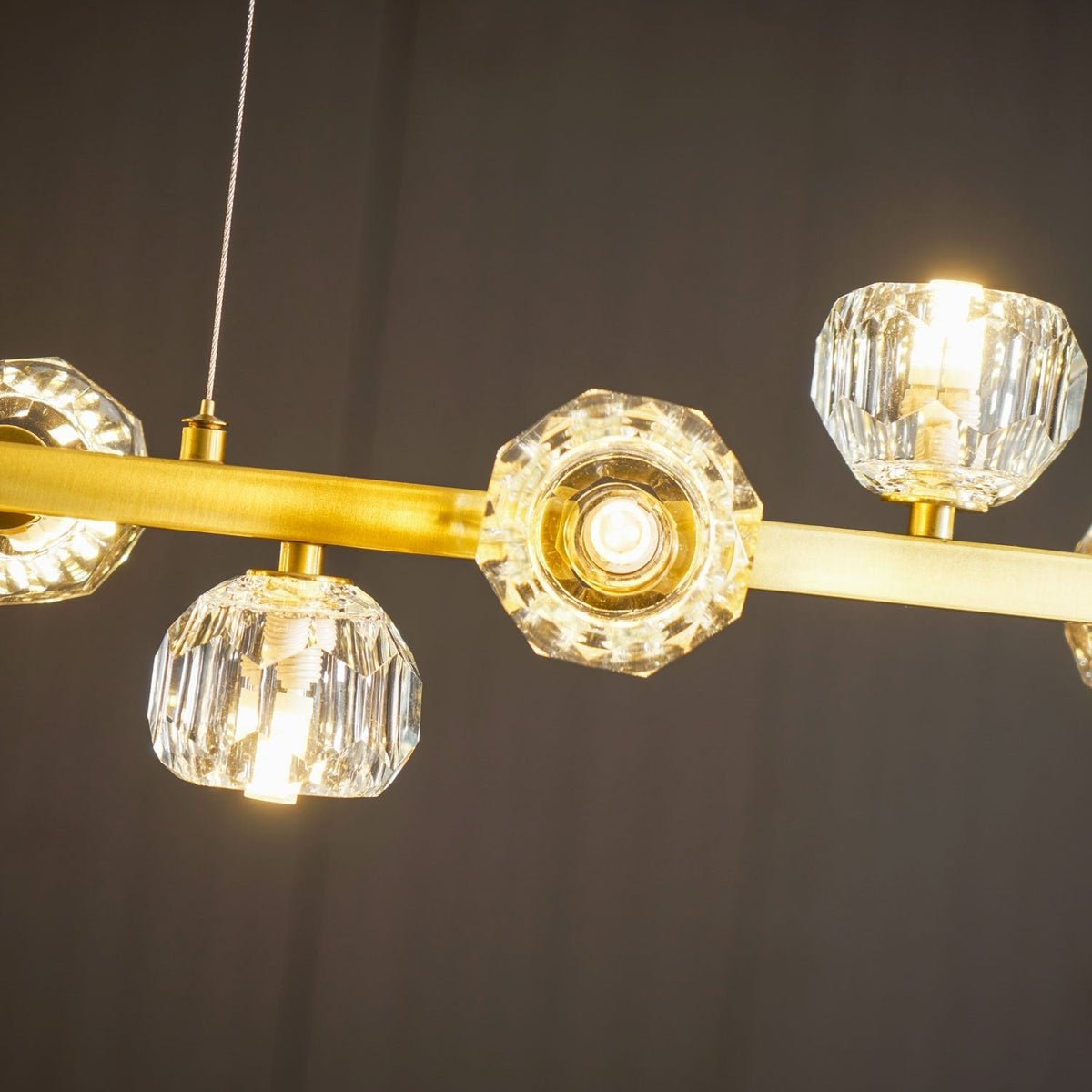 Looking up at the lit crystal balls and the thin hanging cord on the brass bar of this Clérachic chandelier.