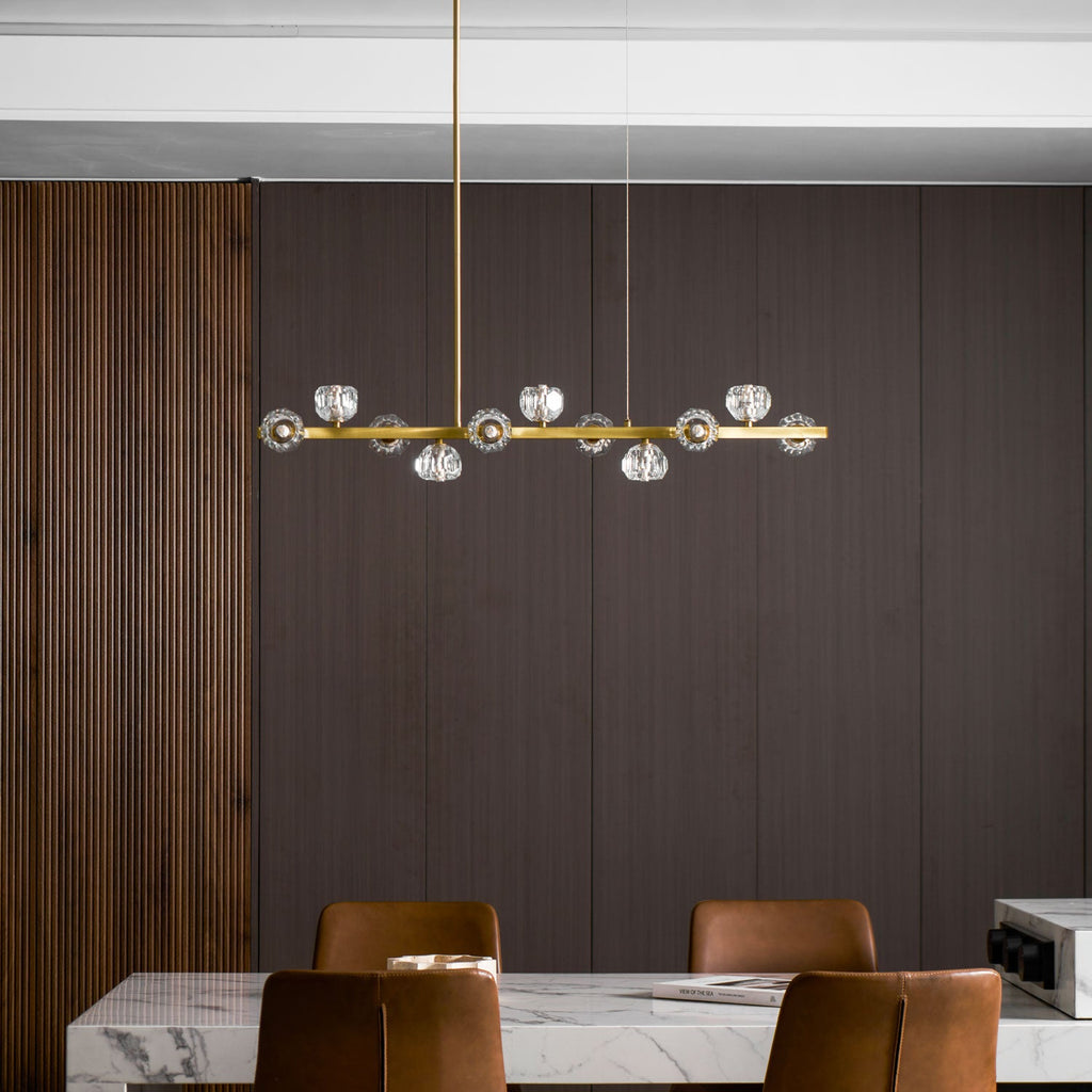 Brass bar of crystal balls over a marble dining table and tan chairs, a Clérachic chandelier against smooth brown panelling.