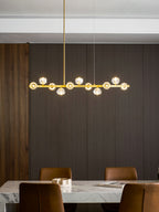 This Clérachic chandelier lit warmly over a marble dining table, its crystal balls glowing along the brass bar.