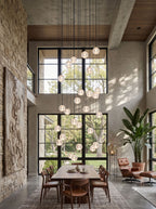 A tall fall of Clérachic crystal balls in a double-height room with a stone wall, black-framed windows and a dining table below.