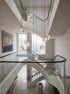 Clérachic crystal ball pendants at several heights inside a pale stairwell, seen over a glass balustrade with a blue painting beyond.