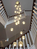 Looking up a white staircase to a round ceiling plate with Clérachic crystal ball pendants hanging in a glowing cluster.