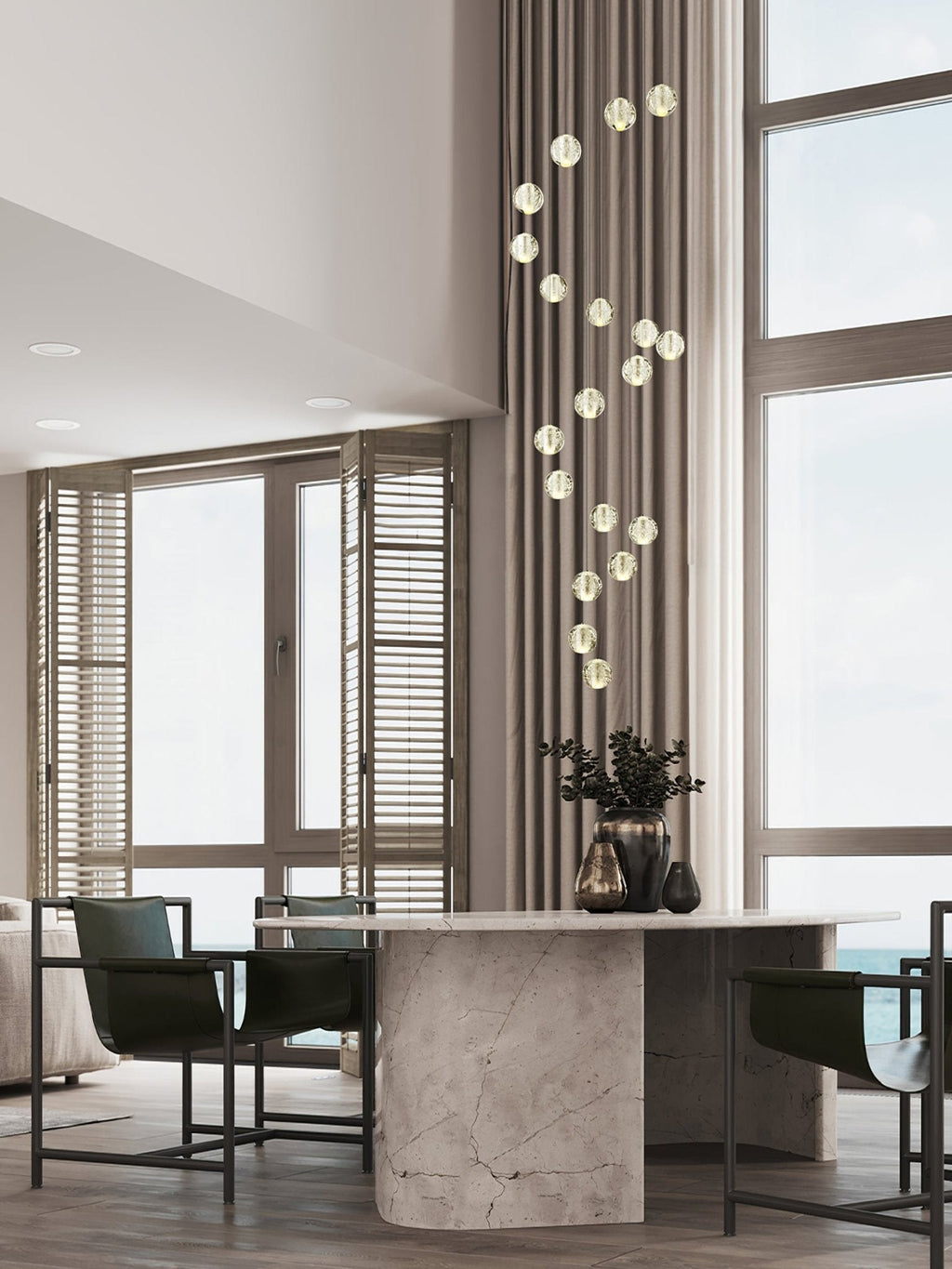 A slim spiral of Clérachic crystal balls hanging beside a tall window above a stone dining table with dark chairs.