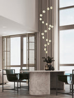 A slim spiral of Clérachic crystal balls hanging beside a tall window above a stone dining table with dark chairs.