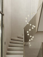 Clérachic crystal ball pendants hanging in a loose spiral beside a pale concrete staircase with a glass balustrade.