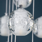 Close view of one Clérachic crystal ball, a clear glass sphere with tiny trapped bubbles around a frosted core and a chrome cap.