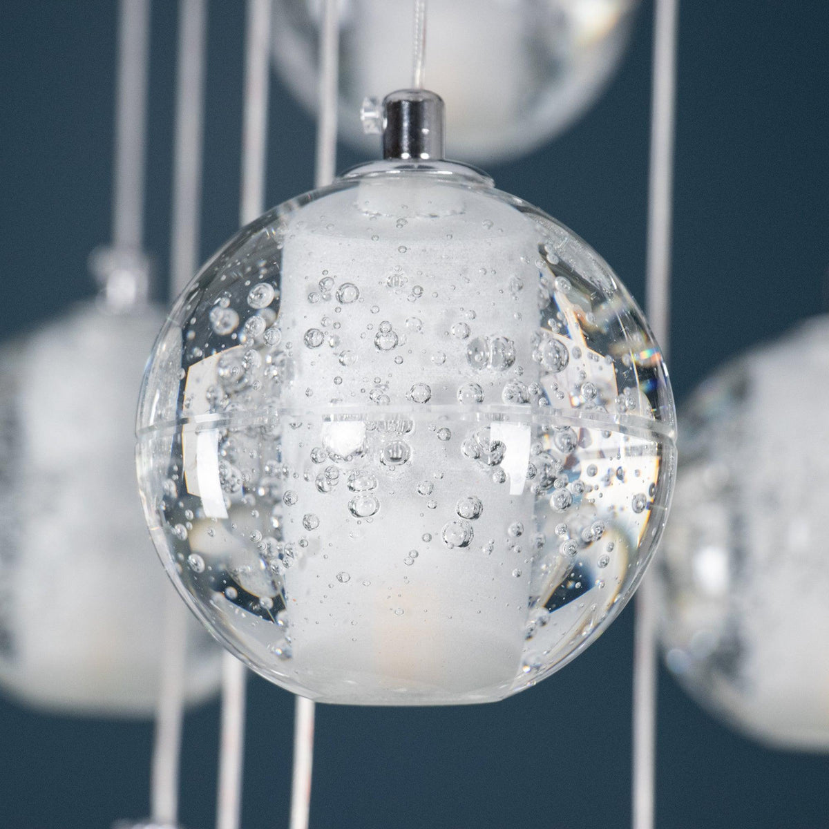 Close view of one Clérachic crystal ball, a clear glass sphere with tiny trapped bubbles around a frosted core and a chrome cap.