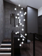Clérachic crystal ball pendants lit in a dark stairwell, hanging at many heights beside black walls and a lit staircase.