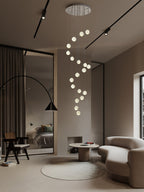 Clérachic crystal ball pendants in a spiral from a round ceiling plate, in a high room with black track lights and an arc floor lamp.