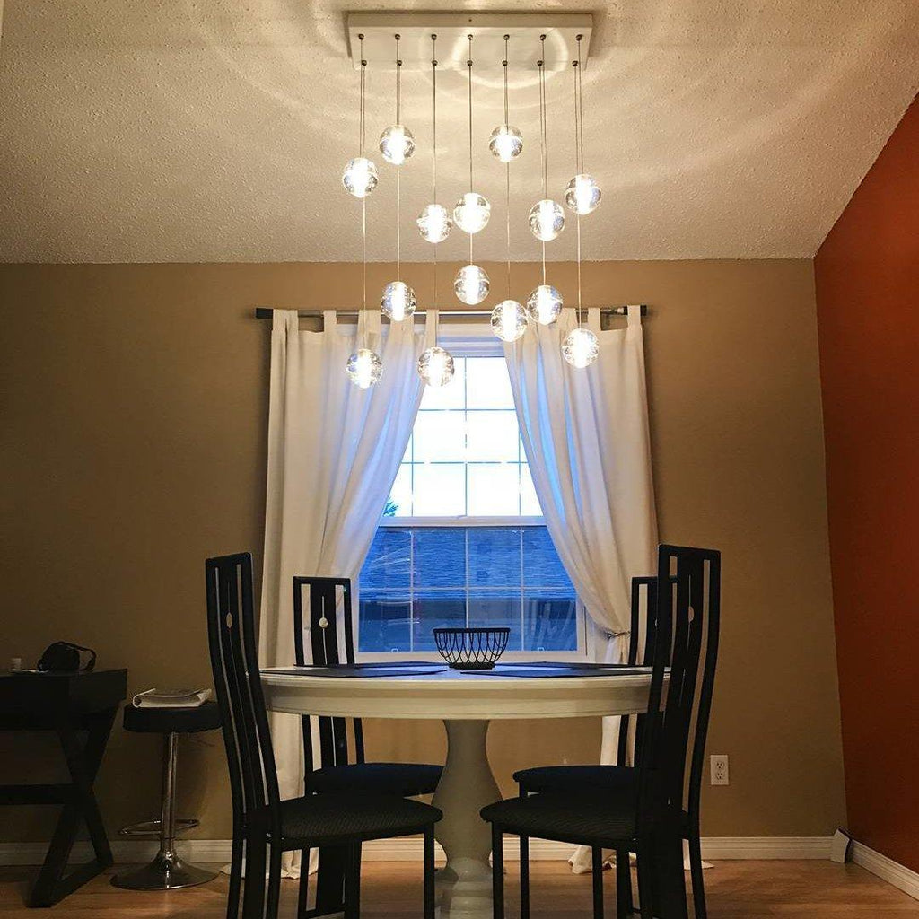 A rectangular canopy with Clérachic crystal balls glowing at different heights over a round dining table and black chairs.