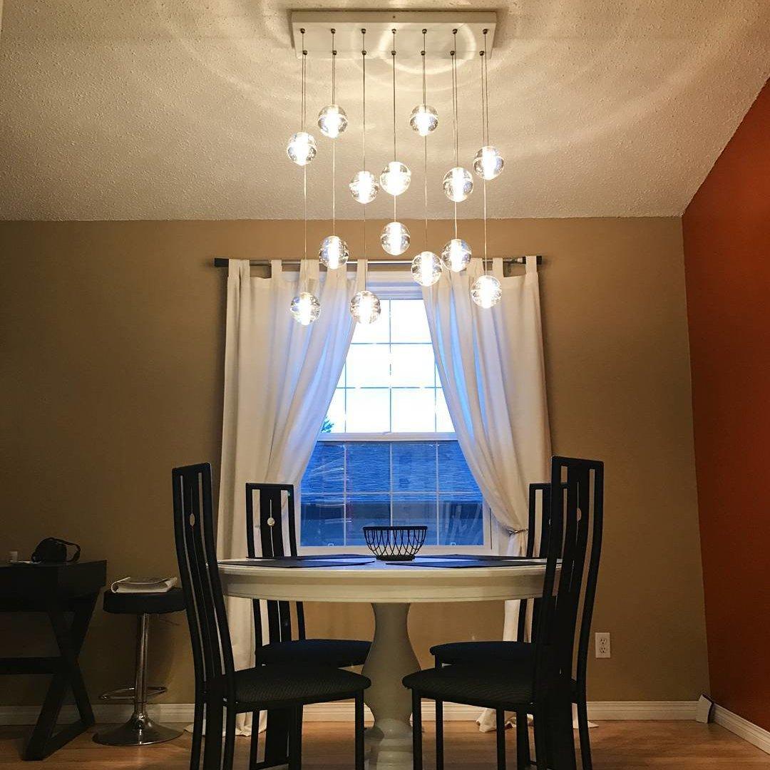 A rectangular canopy with Clérachic crystal balls glowing at different heights over a round dining table and black chairs.