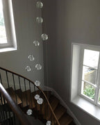 Clérachic crystal ball pendants hanging in a tall spiral down a stairwell with two windows and a curved wooden handrail.