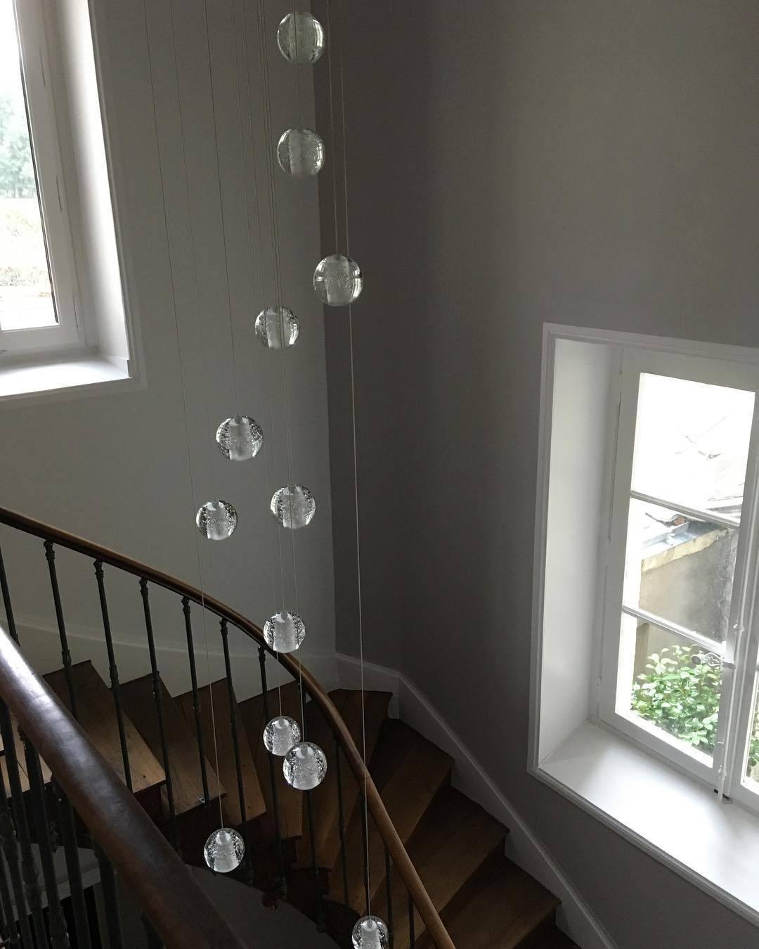 Clérachic crystal ball pendants hanging in a tall spiral down a stairwell with two windows and a curved wooden handrail.
