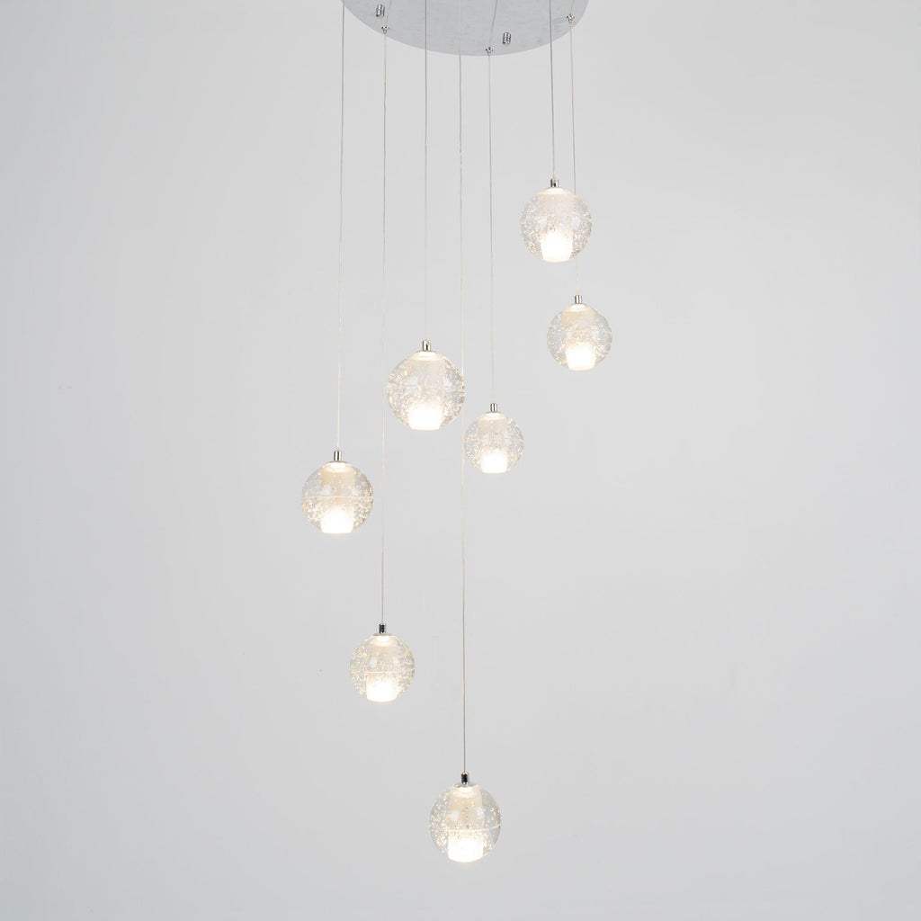 Clérachic crystal ball pendants lit warm on a pale grey backdrop, hanging from a round chrome ceiling plate at varied heights.