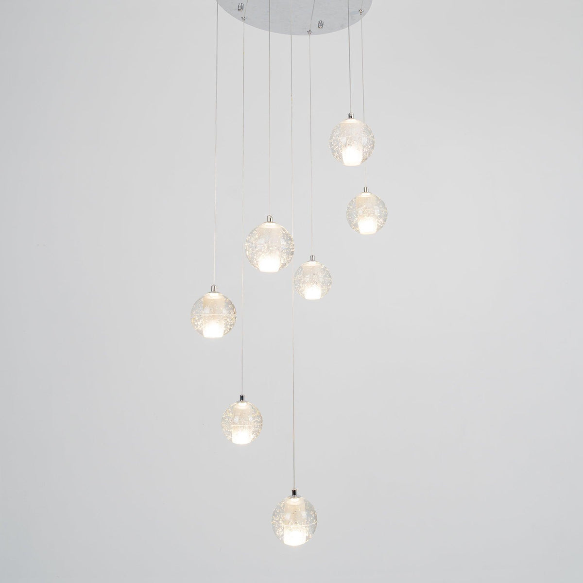 Clérachic crystal ball pendants lit warm on a pale grey backdrop, hanging from a round chrome ceiling plate at varied heights.