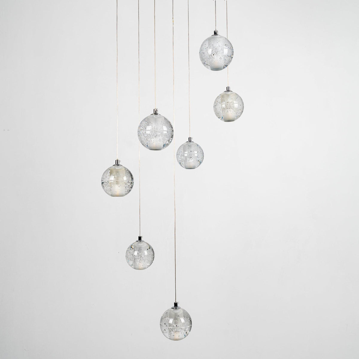 Clérachic crystal ball pendants unlit against pale grey, the clear bubbled spheres hanging at different heights on thin cables.