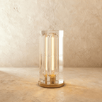 Clérachic tall rectangular crystal table lamp on a round gold-tone base, glowing warm, on a limewash wall and stone surface.