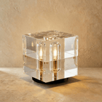 Clérachic compact crystal cube table lamp with lit capsule bulbs in its faces, standing on a dark round base.