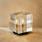 Clérachic larger crystal cube table lamp with warm capsule bulbs glowing inside clear glass, on a black round base.