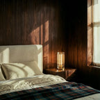 Clérachic tall crystal table lamp glowing on a walnut bedside table beside a cream headboard in a wood-panelled bedroom.