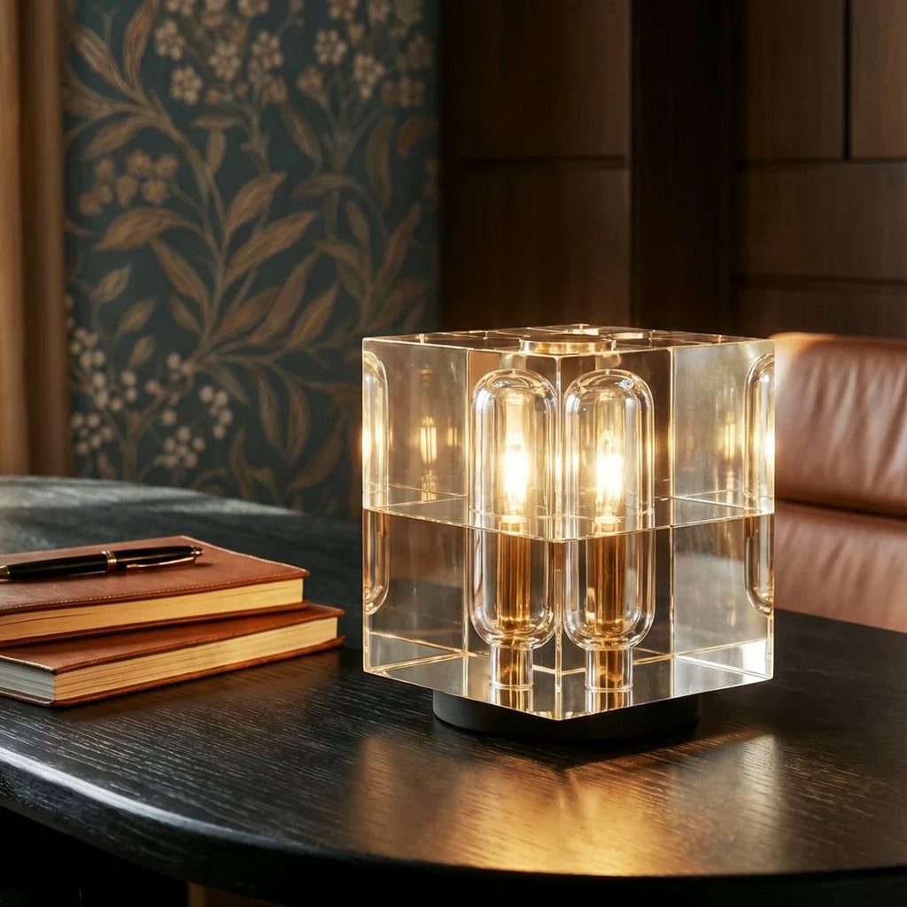 Clérachic crystal cube table lamp glowing on a dark wooden table next to leather-bound notebooks and a pen.