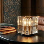 Clérachic crystal cube table lamp glowing on a dark wooden table next to leather-bound notebooks and a pen.