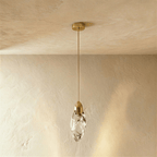 Clérachic single clear glass teardrop pendant with a brushed brass cap, rod and round canopy, against a limewash wall.