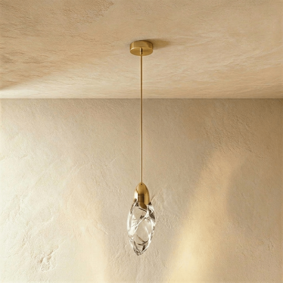 Clérachic single clear glass teardrop pendant with a brushed brass cap, rod and round canopy, against a limewash wall.