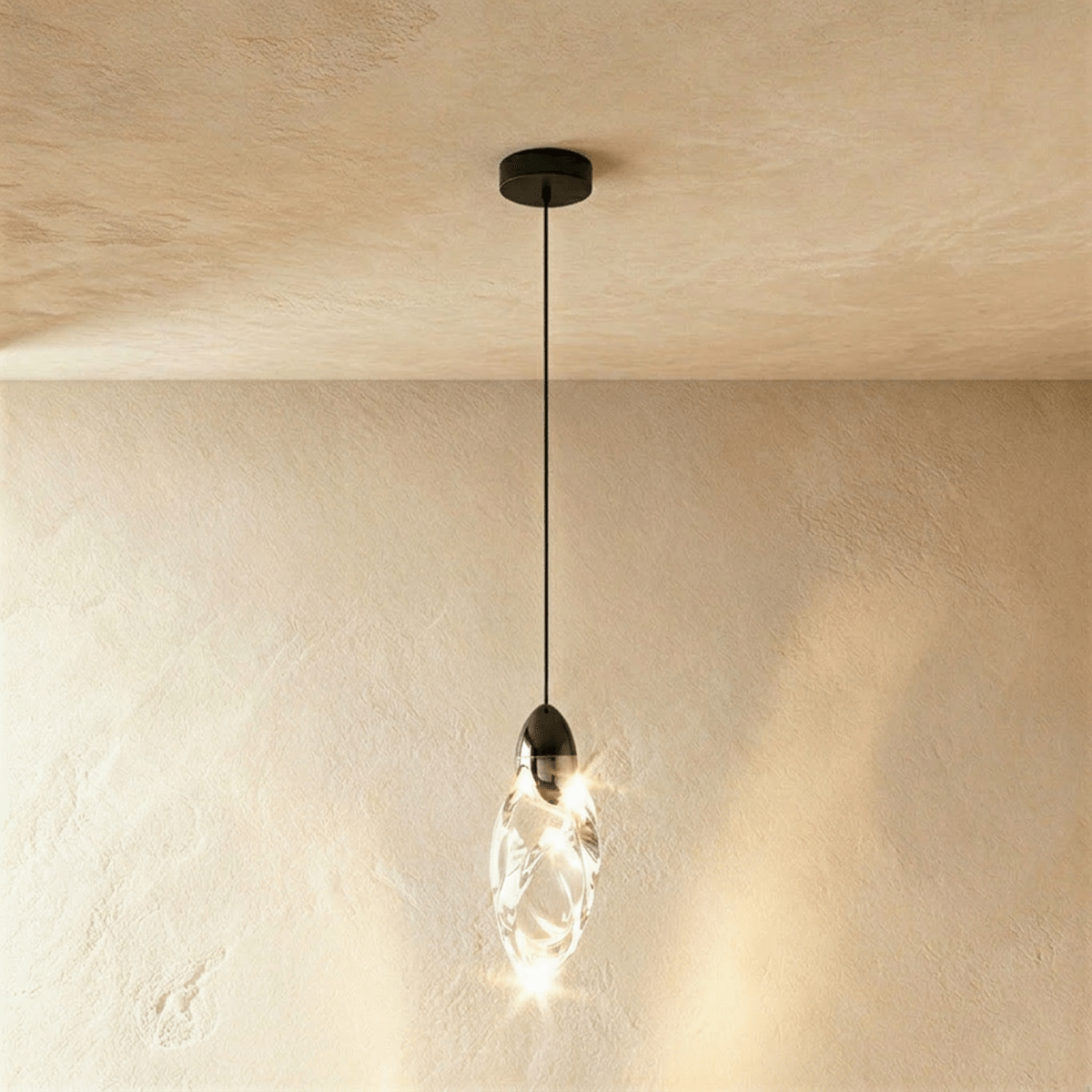 Clérachic single twisted clear glass pendant lit warm, with a black cap, cord and round canopy against limewash plaster.