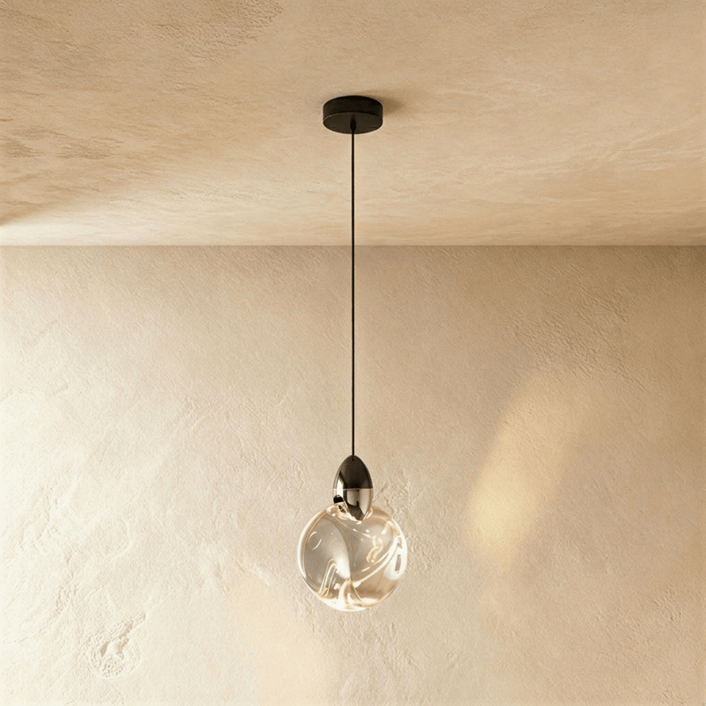Clérachic round rippled clear glass pendant with a dark metal cap on a black cord and canopy, against a warm plaster wall.