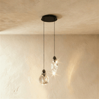 Clérachic pair of clear glass pendants, one round and one teardrop, on black cords from a round black canopy.