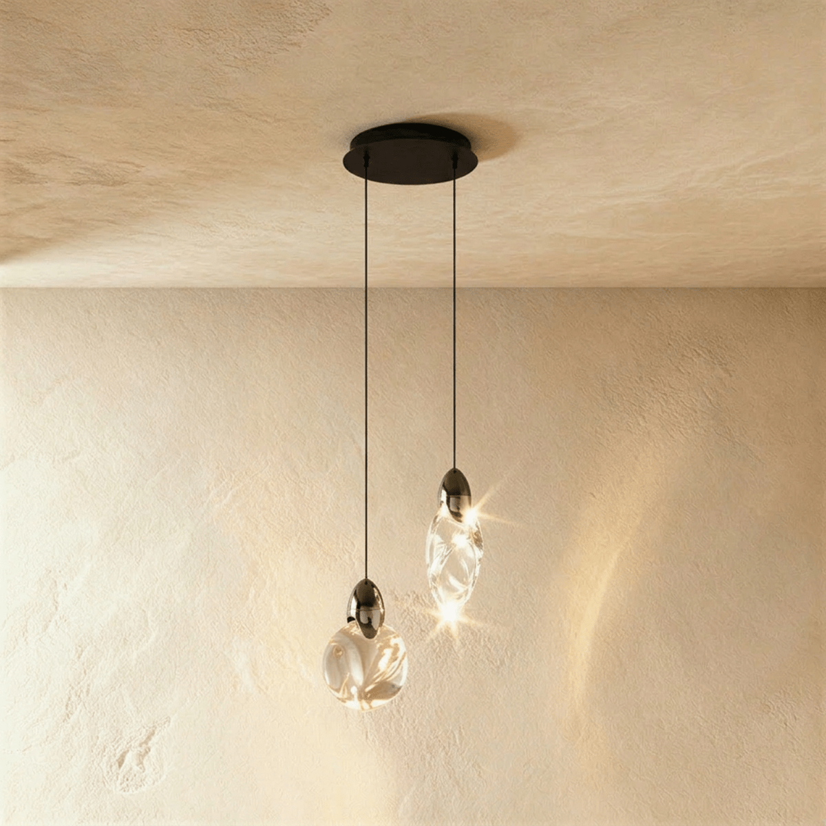 Clérachic pair of clear glass pendants, one round and one teardrop, on black cords from a round black canopy.