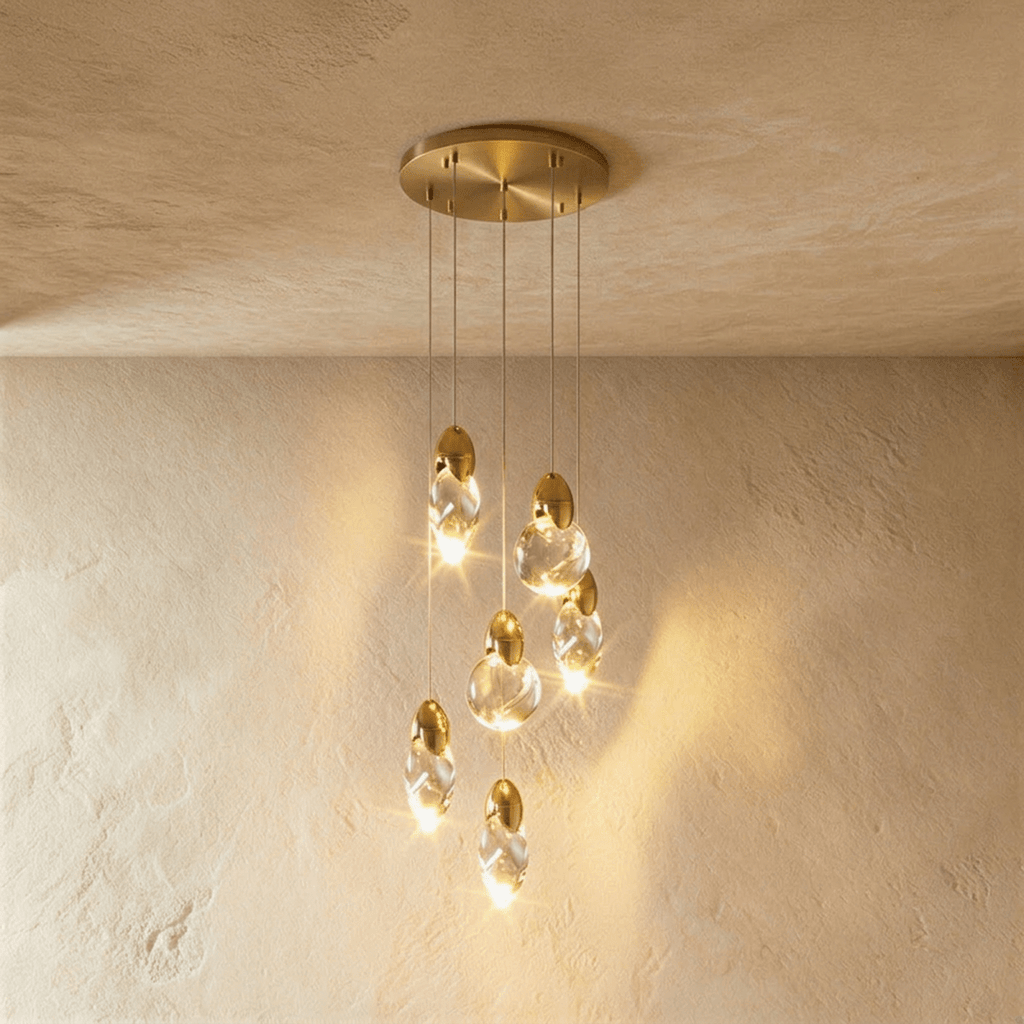 Clérachic cluster of six glowing clear glass pendants at staggered heights from a round brass canopy over plaster.