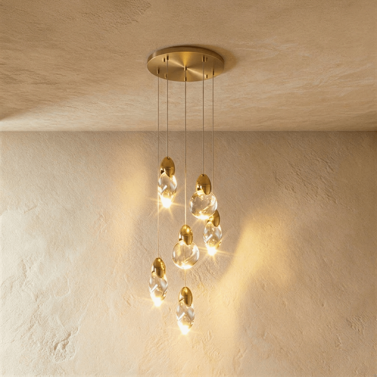 Clérachic cluster of six glowing clear glass pendants at staggered heights from a round brass canopy over plaster.