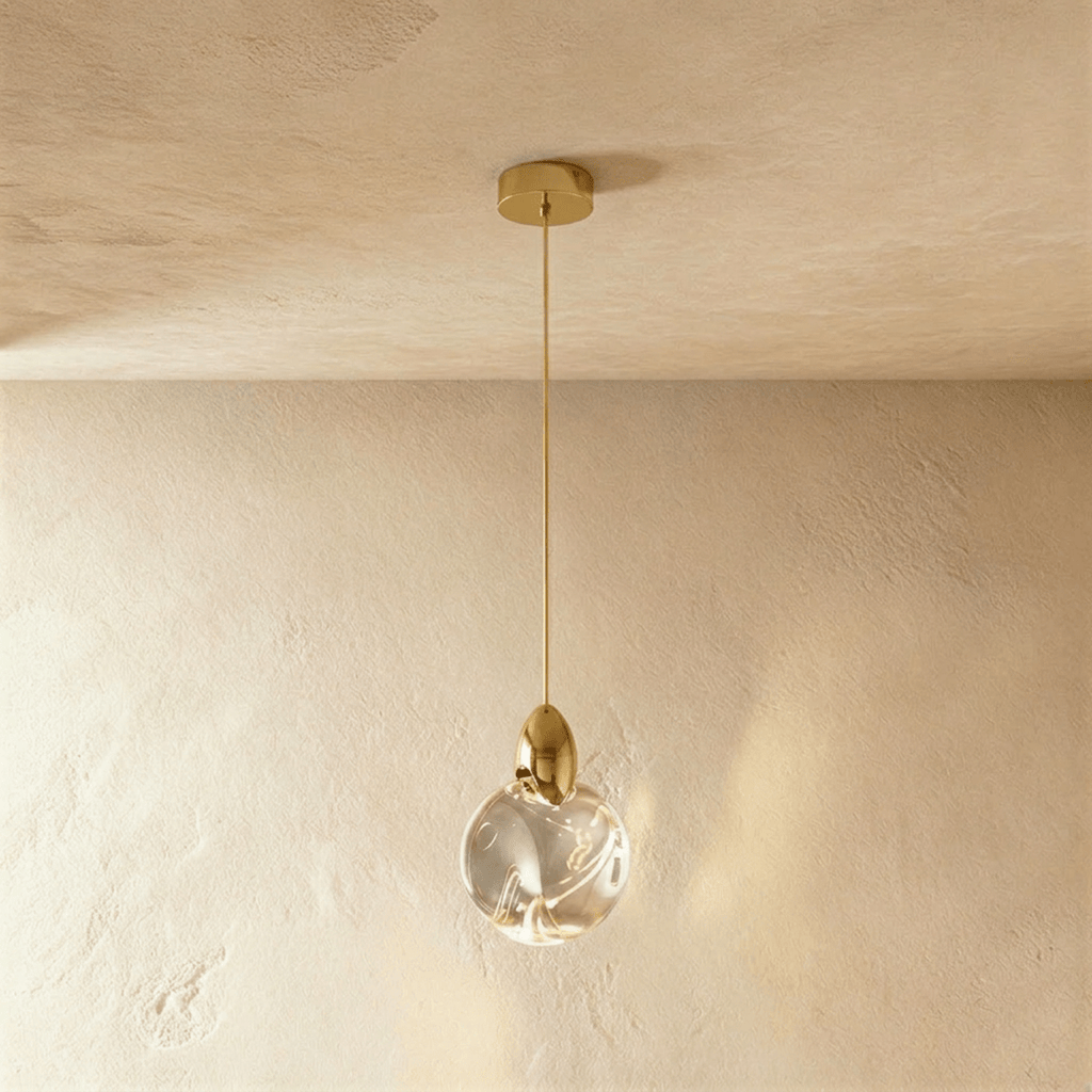 Clérachic round rippled clear glass pendant with a polished brass cap and stem, hanging against a limewash wall.