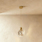 Clérachic round rippled clear glass pendant with a polished brass cap and stem, hanging against a limewash wall.