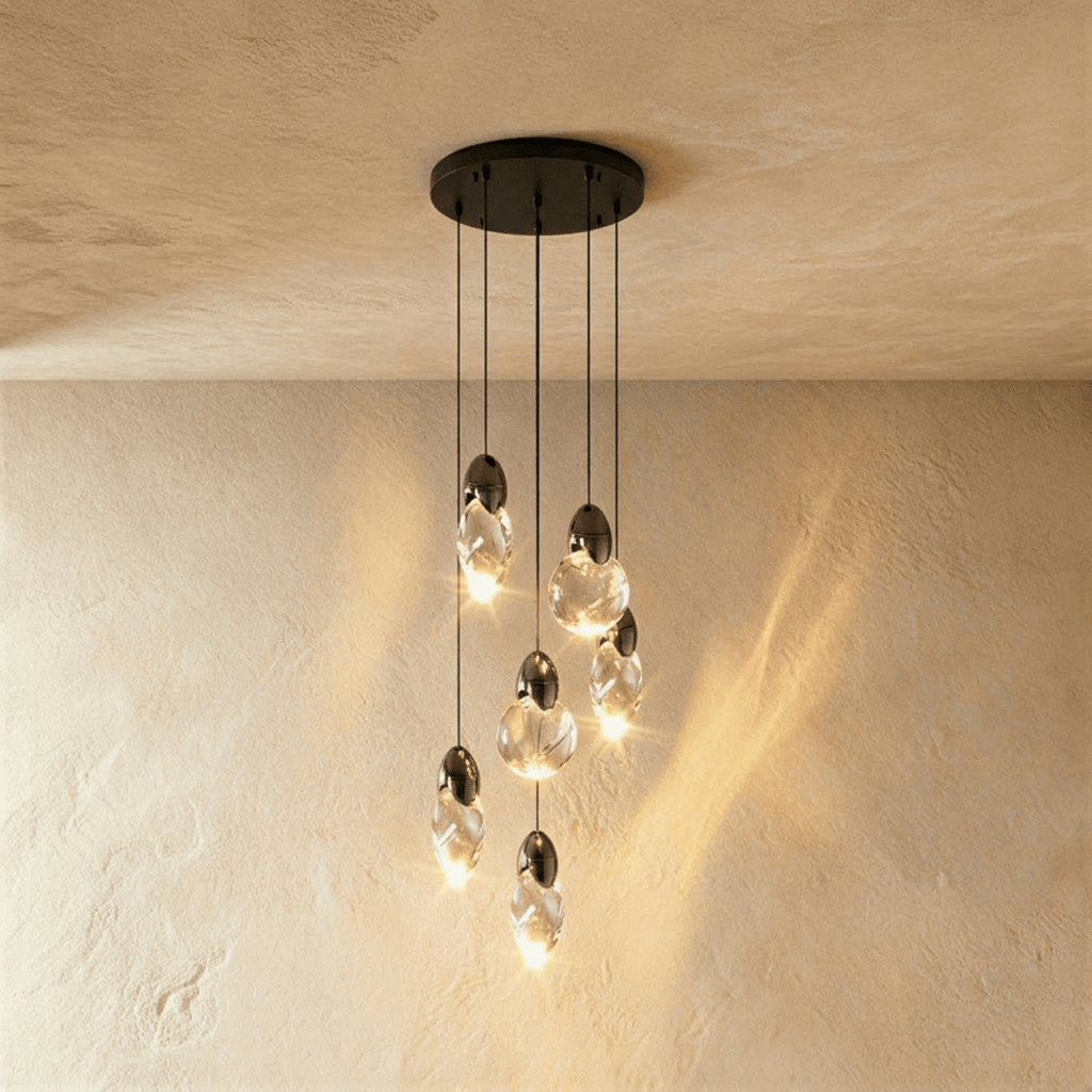 Clérachic cluster of six clear glass pendants with dark caps at staggered heights from a round black canopy.