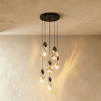Clérachic cluster of six clear glass pendants with dark caps at staggered heights from a round black canopy.