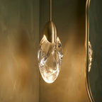 Close view of a Clérachic rippled glass teardrop pendant lit warm, with a brushed brass cap and braided cord.