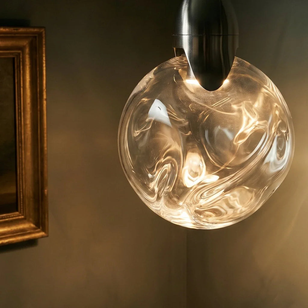 Close view of a Clérachic round glass pendant with swirling ripples and a brushed steel cap, lit warm against a dark wall.