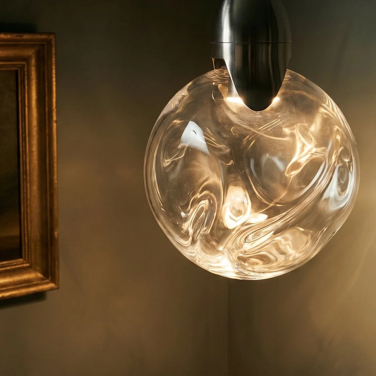 Close view of a Clérachic round glass pendant with swirling ripples and a brushed steel cap, lit warm against a dark wall.