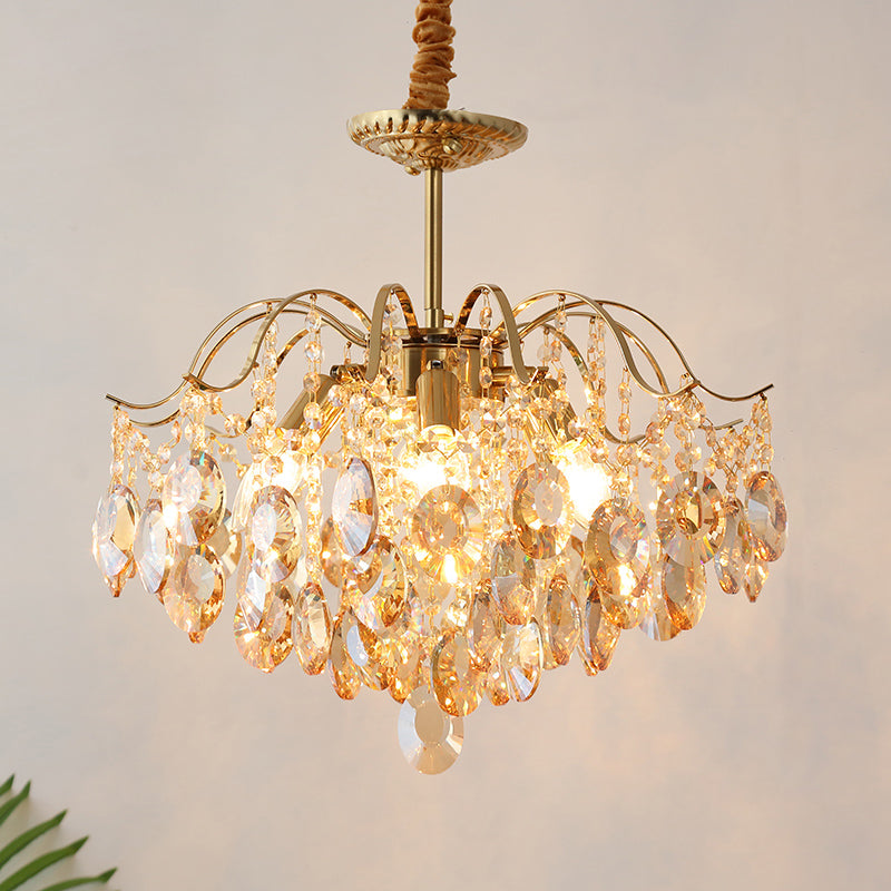Lit Clérachic chandelier with amber teardrop crystals under a gold canopy, hung from a fabric-wrapped cord against a pale wall.