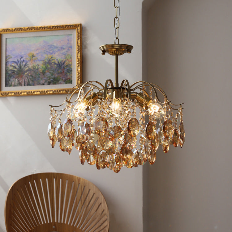 Clérachic chandelier with warm amber crystals hanging beside a gilt-framed landscape painting and a woven wooden chair back.