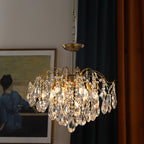 Clear crystal drops on this Clérachic gold chandelier, with a framed painting and dark curtains in the background.