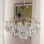 Clear teardrop crystals on a brass-finished frame, this Clérachic chandelier hung against a window with a pale curtain.