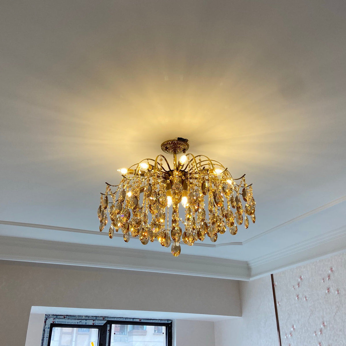 Small Clérachic chandelier lit on a ceiling, casting a starburst of warm light over the white ceiling and cornice.